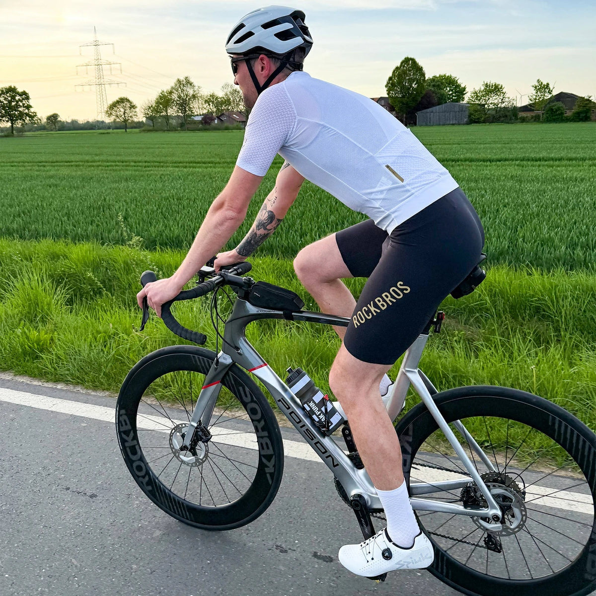 Ein Radfahrer im weißen Trikot und schwarzer Trägerhose auf einer Landstraße.