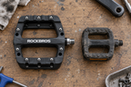 Plattformpedale Nylon – breites Pedal neben einem alten schmalen Pedal auf der Werkbank